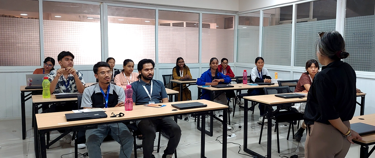 An instructor faces eight students seated at desks, each using a laptop.